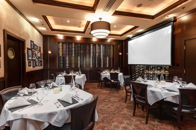 VIEW OF THE PRIVATE DINING ROOM IN MIAM WITH THE PROJECTION SCREEN DOWN AND CRESCENT ROUND TABLES SETUP