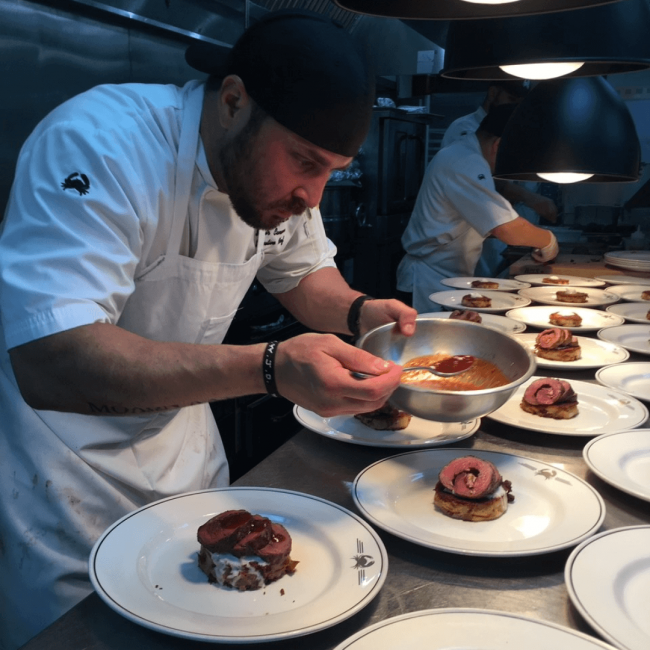 chef Sammy plating up a wine dinner in the kitchen holding a bowl with sauce