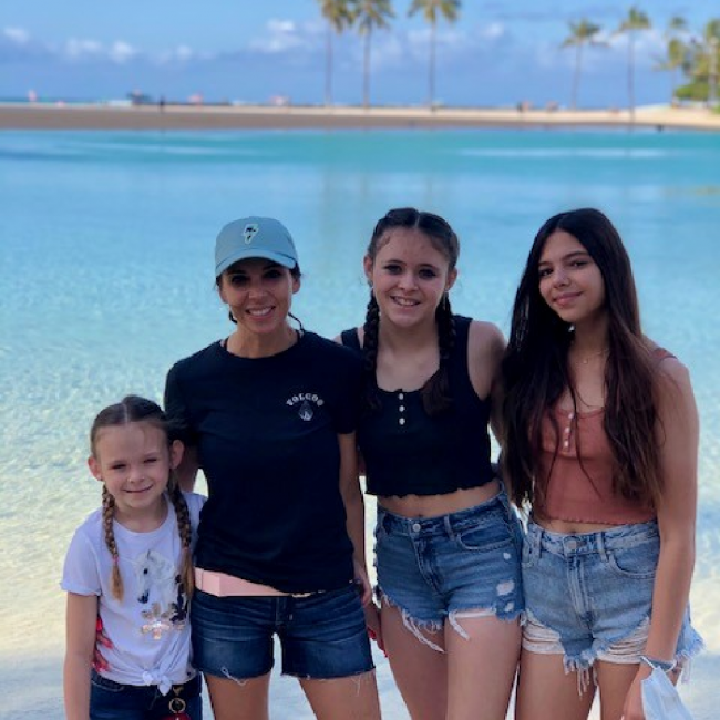 Tambra with her daughters at the beach with blue ocean water and palm trees in the background