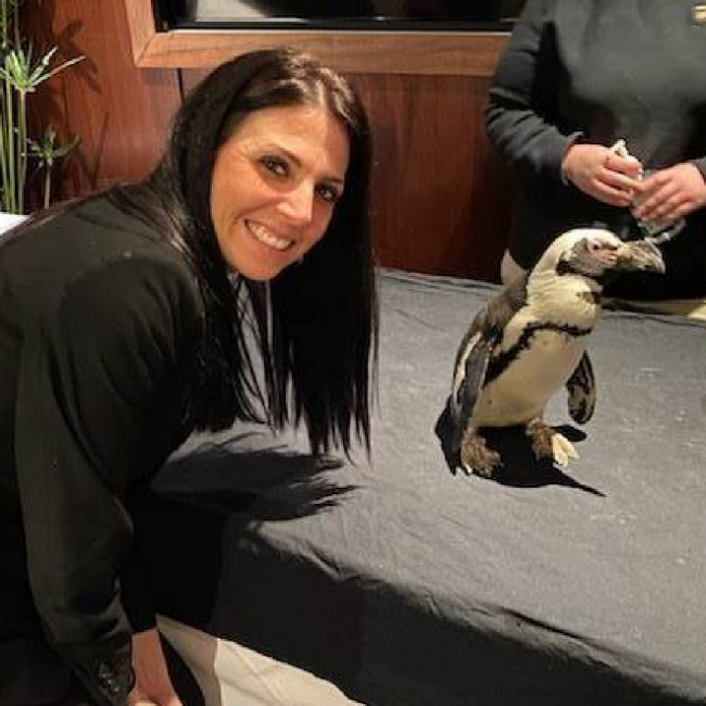 Tambra smiling next to a penguin from the Dallas Zoo at an event held in the private dining room