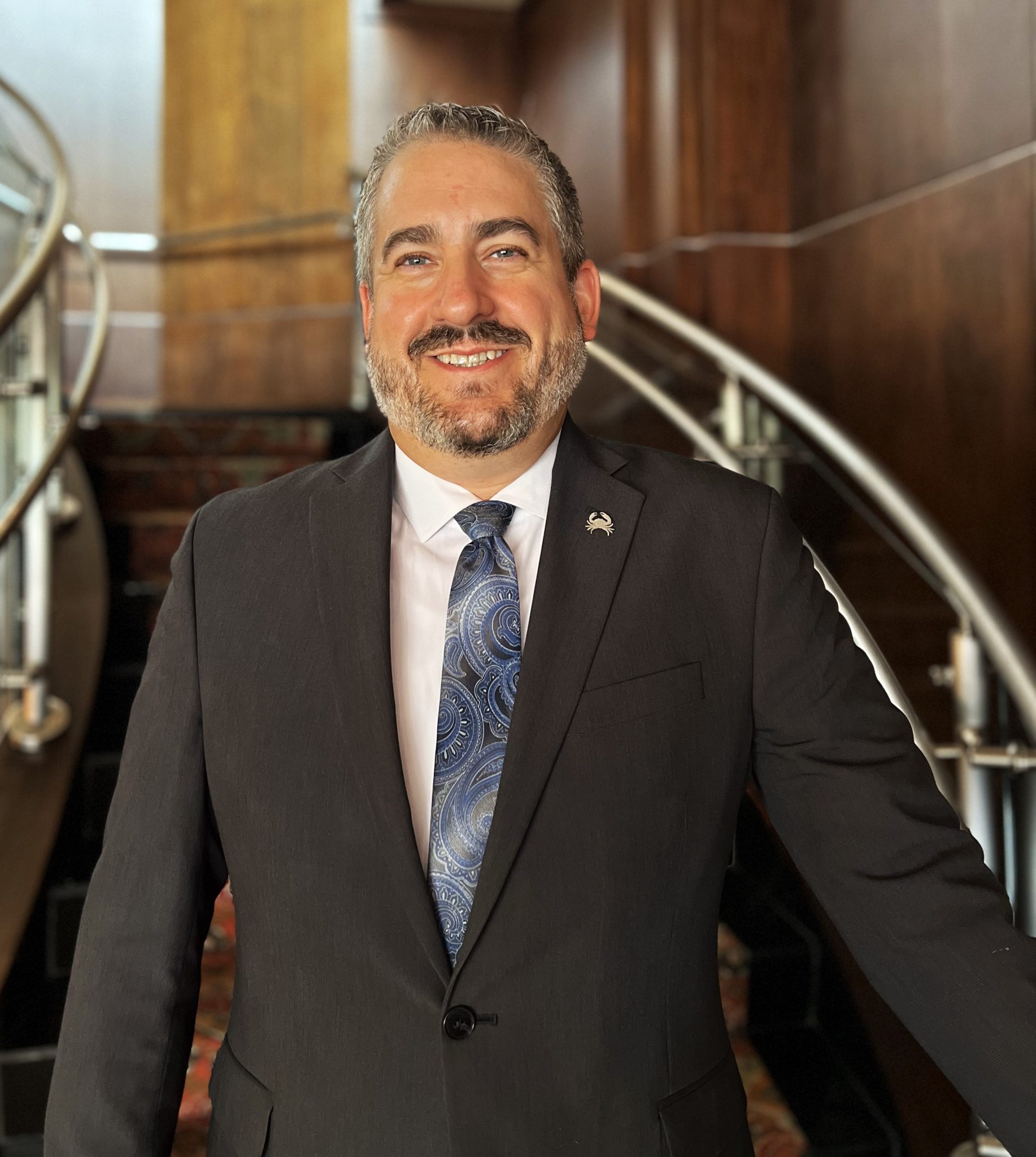 headshot of Ryan Studt general manager of Truluck's Dallas in a dark gray suite with white shirt and blue tie standing at the bottom of the staircase
