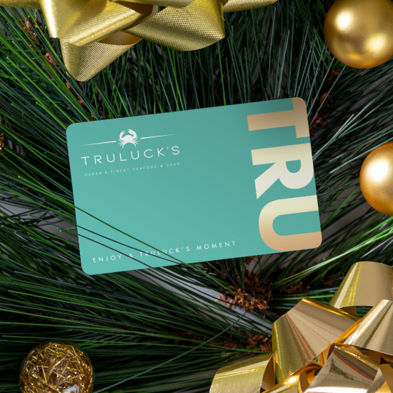 Truluck's gift card in blue and gold on top of holiday greenery with gold bows and ornaments