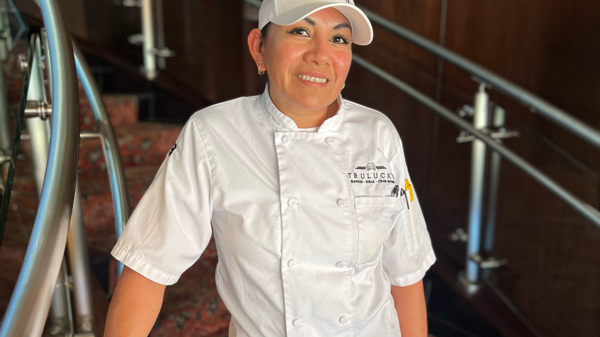 DFW pastry chef Paula Delgado in her chef coat and hat on the staircase in Dallas