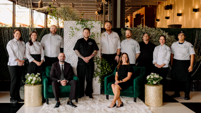 Team Woodlands private dining team seated and standing on the Terrace with floral decor and green velvet chairs
