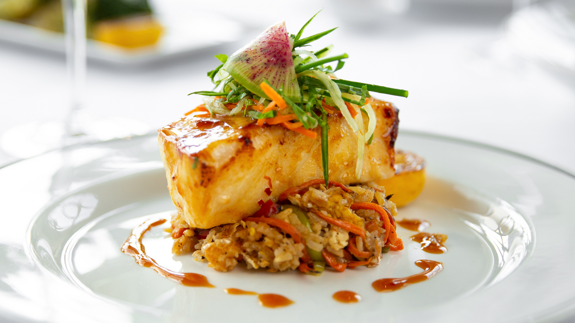 miso glazed seabass over crab fried rice with chilled cucumber slaw and a watermelon radish on a white plate