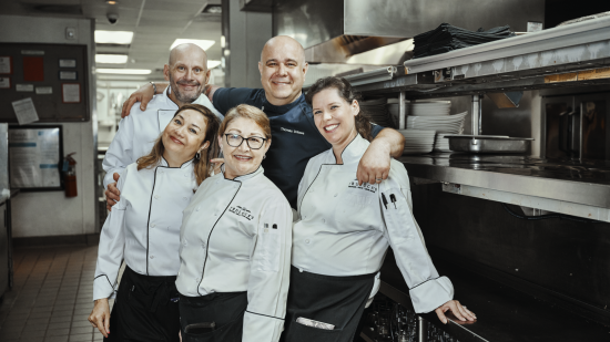 Chef Thomas with a few Houston team servers smiling and grouped together in the back of house kitchen area