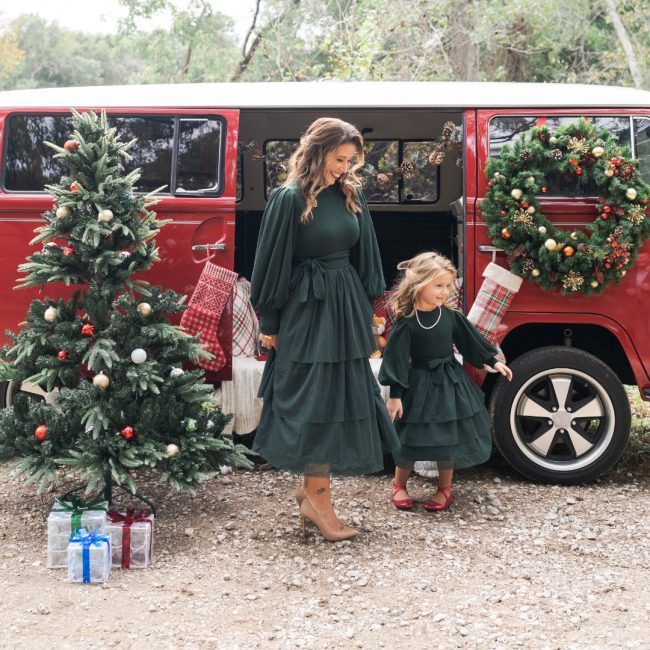 Amber and her daughter in green dresses in front of a red VW van with a Christmas tree and wreath in the background