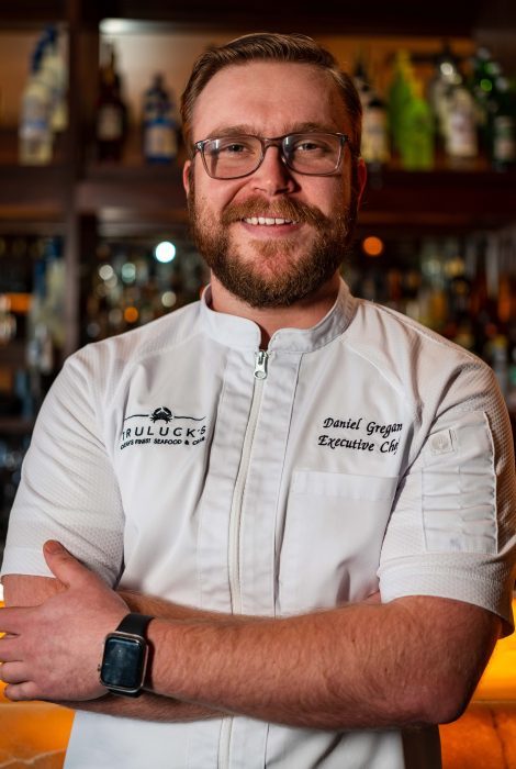 Chef Dan Gregan in a white logo chef coat with his arms folded in front of the bartop