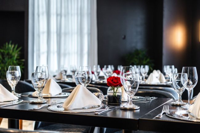 private Trident room at Truluck's Plano setup with navy leather chairs, black table tops, white linen napkins, glassware, red roses and green plants in the background