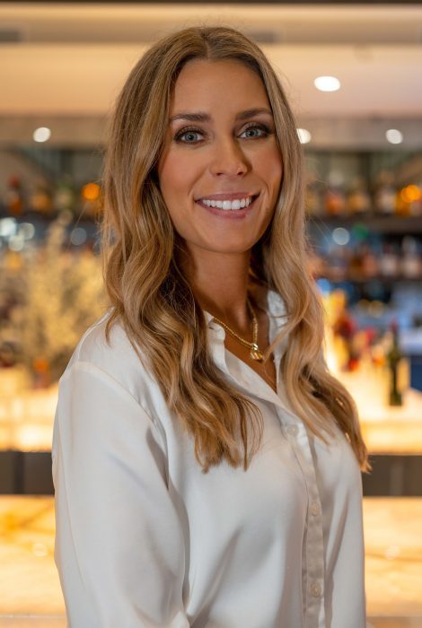 sales manager Vanessa Sbraga smiling in front of the back lit bar top in a white blouse