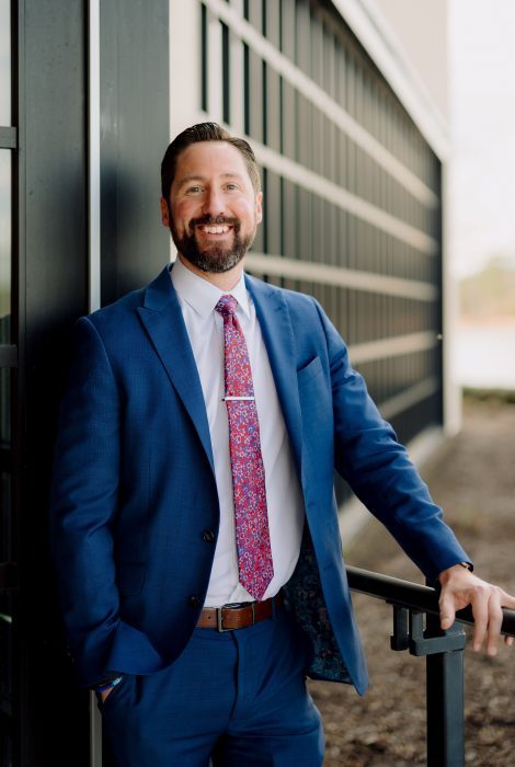 headshot of operating partner, Chris Davis in a blue suit with floral tie standing with his hand on a railing in front of the Truluck's Woodlands location