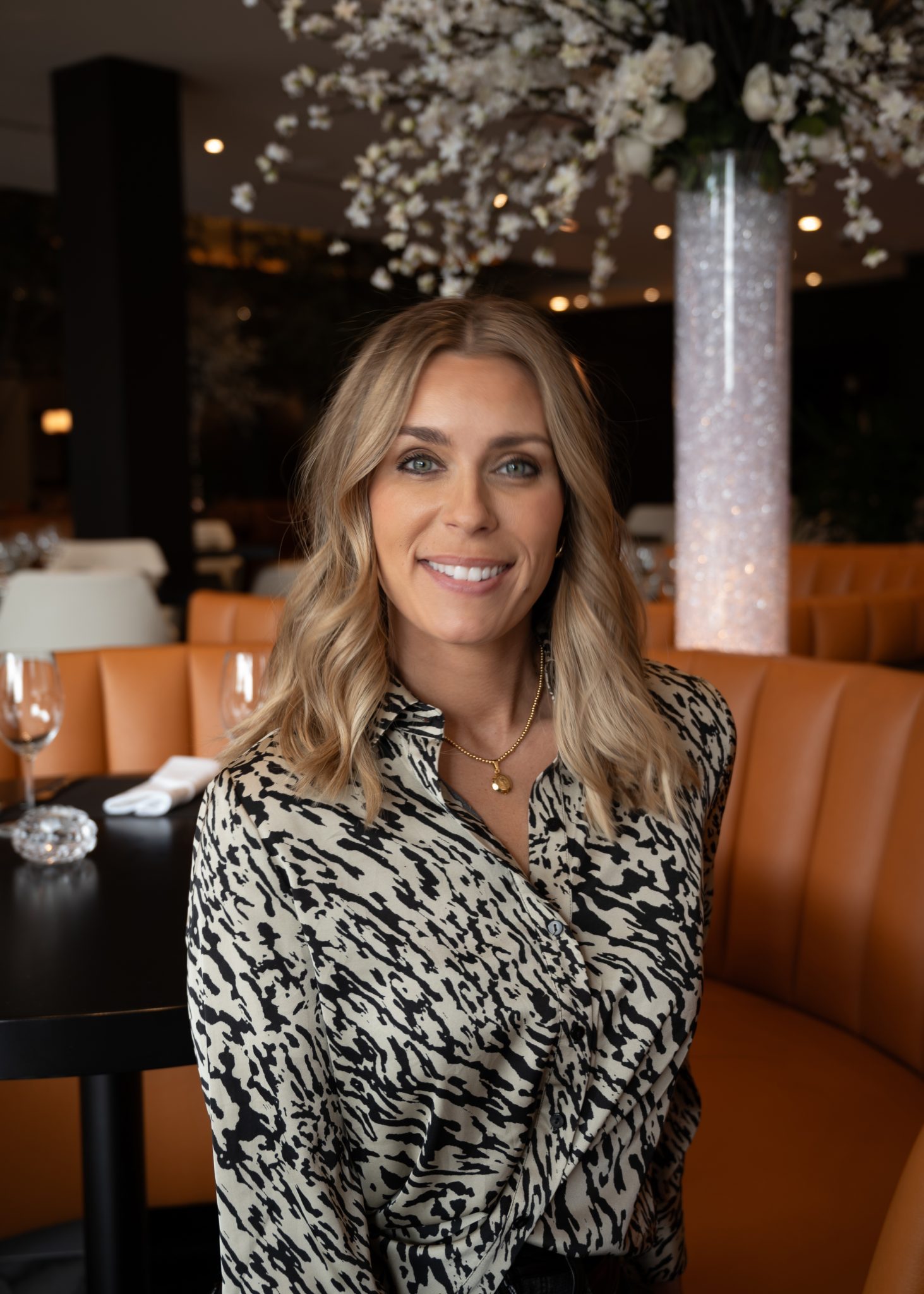 headshot of Vanessa in a print blouse in the main dining room with a large floral tube in the background