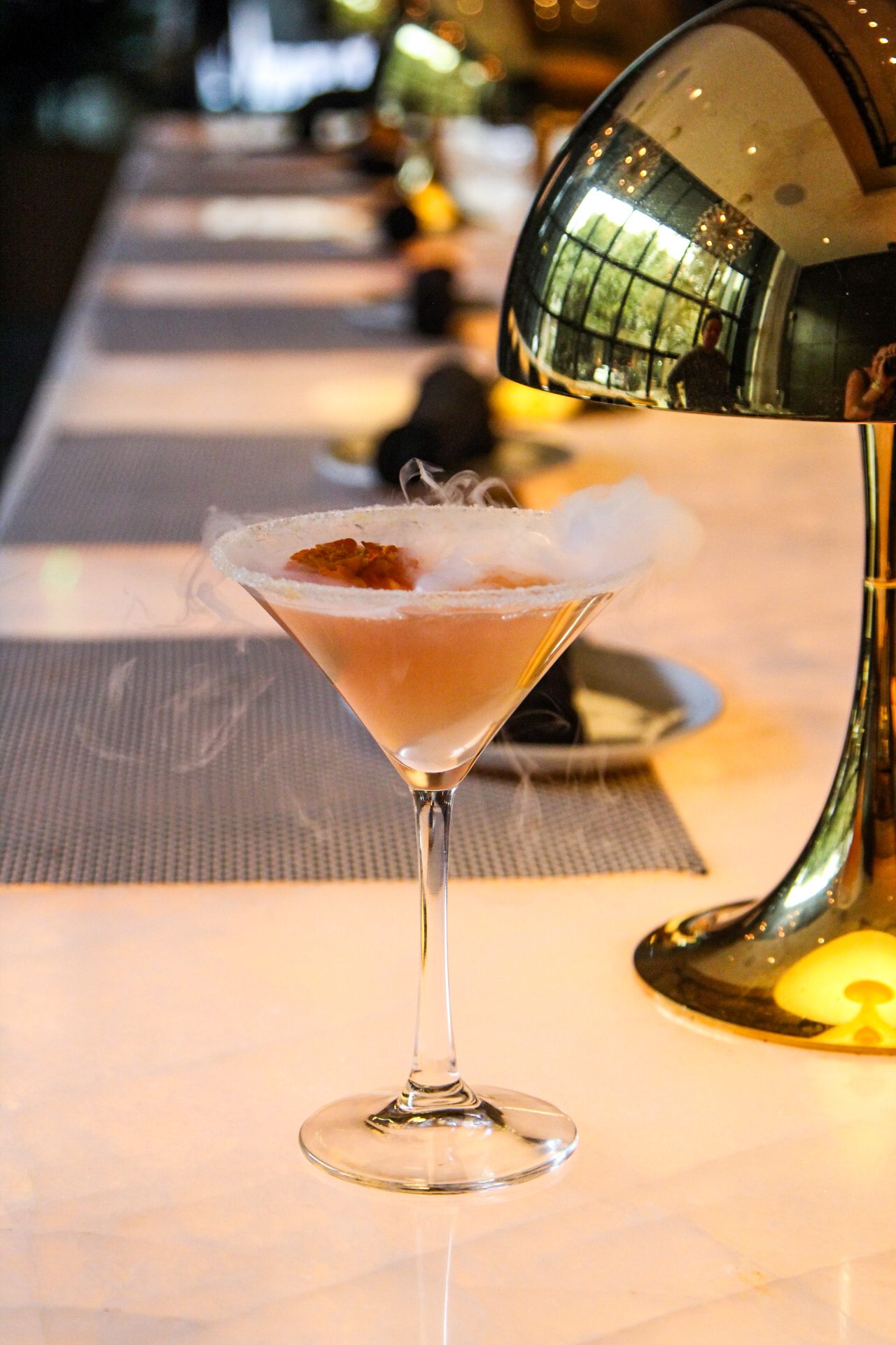 smoking Voila! cocktail on the bar top with a gold lamp in the background