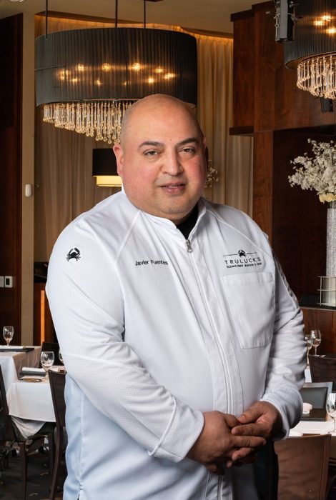 Chef Javier Fuentes in a chef coat int he dining room with chandeliers and floral in the background