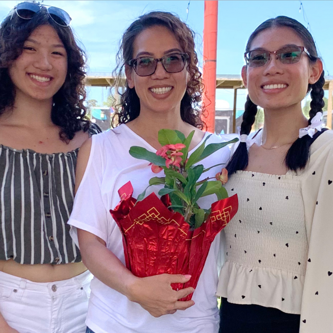 Ivy holding a flowering plant and her two daughters