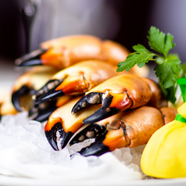 stone crab claws piled high on top of a bed of crushed ice with a sprig of parsley and a wrapped lemon