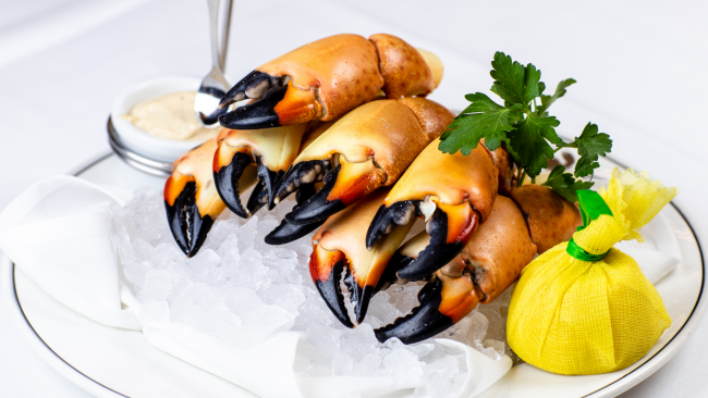 stone crab claws stacked up on a bed of ice with a ramekin of spicy mustard and a lemon wrapped