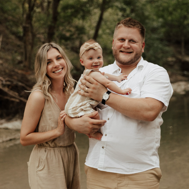 Jordan with his wife and baby posing in the outdoors in front of a river
