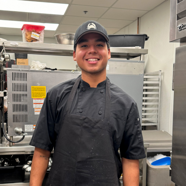 photo of Mauricio in uniform with a Truluck's hat in the kitchen area of the restaurant
