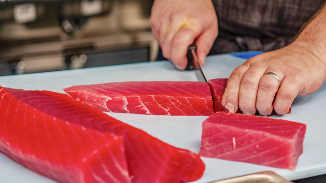 raw whole tuna being cut by Chef on a cutting board