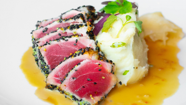 close up image of sesame crusted tuna with mashed potatoes and a parsley garnish over tamari sauce