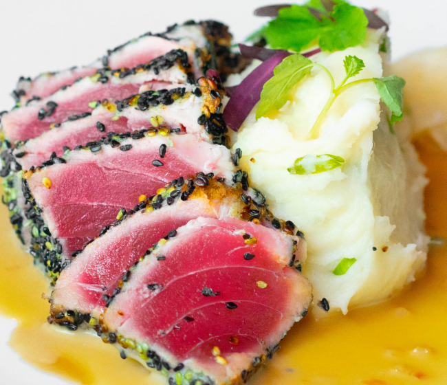 close up image of sesame crusted tuna with mashed potatoes and a parsley garnish over tamari sauce