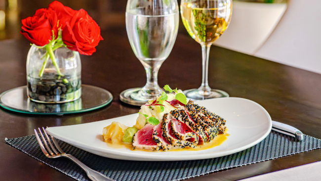 Sesame tuna entree on a tabletop with red roses and a glass of white wine in the background