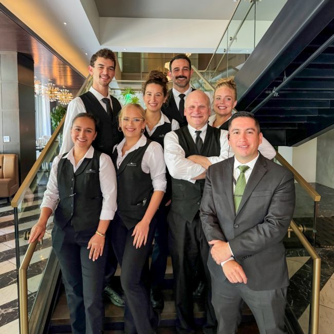 Austin downtown beverage manager, Fernando Nunez, with his bar team posing in front of the staircase