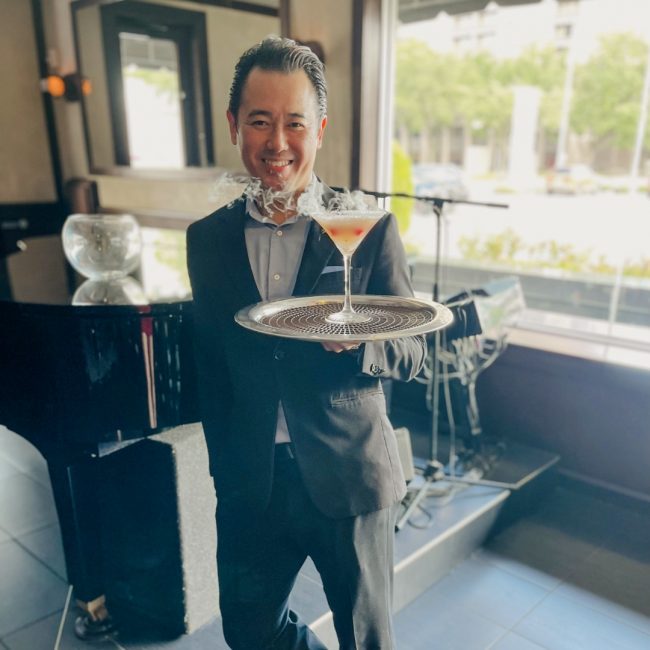 Houston beverage manager, Davis Duong carrying a smoking Voila! cocktail on a tray out to a guest