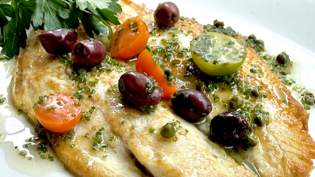 Mediterranean branzino fish topped with heirloom tomatoes, olives, capers and dressed with parsley