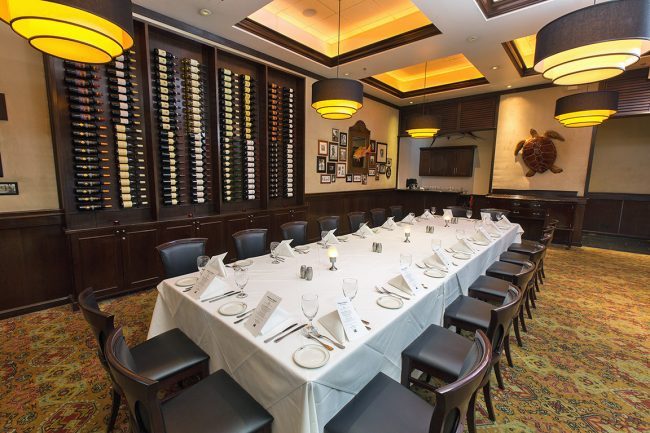 The Houston private Naples Room set up with a boardroom table draped in white linen with a wine wall in the background