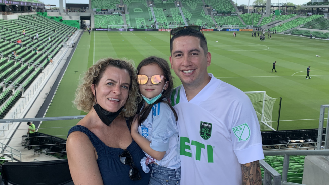 Fern and his family at an Austin FC game with the stadium in the background.