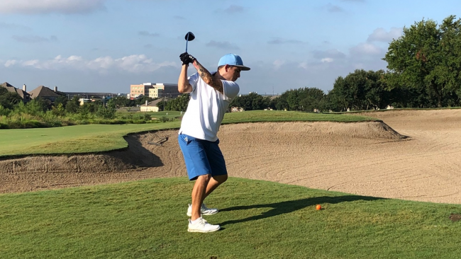 Fernando on the golf course raising his club to swing at the ball by a sand pit.