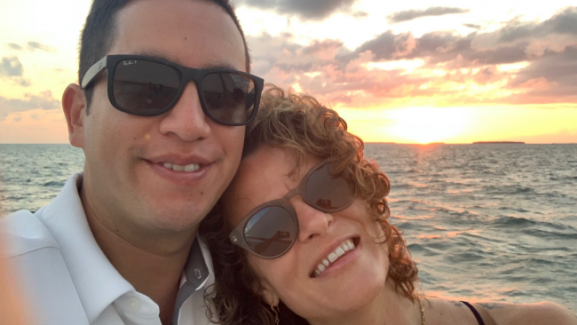 Fern and his wife in sunglasses with the ocean and a beautiful sunset in the background.