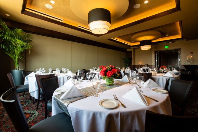 Truluck's Rosemont Pearl Room view from the rear corner looking toward the front of the room. The room is setup with round tables of 8 all dressed in white linen table clothes and red roses.