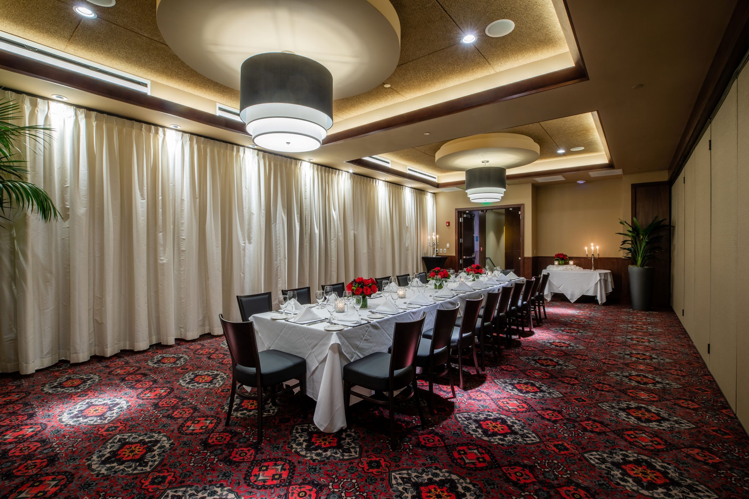 Truluck's Rosemont Naples room view from the far corner of the room facing the entry door. The room is set with a boardroom style table dressed in white linen. The far wall is dressed with white curtains and there is a small buffet table at the front of the room.