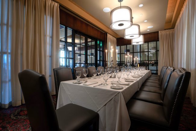 Truluck's Rosemont Big Deal Room view from the far corner of the room looking across to the entry doors. The room is set with a long boardroom style table with high back leather chairs and white linen tablecloths.