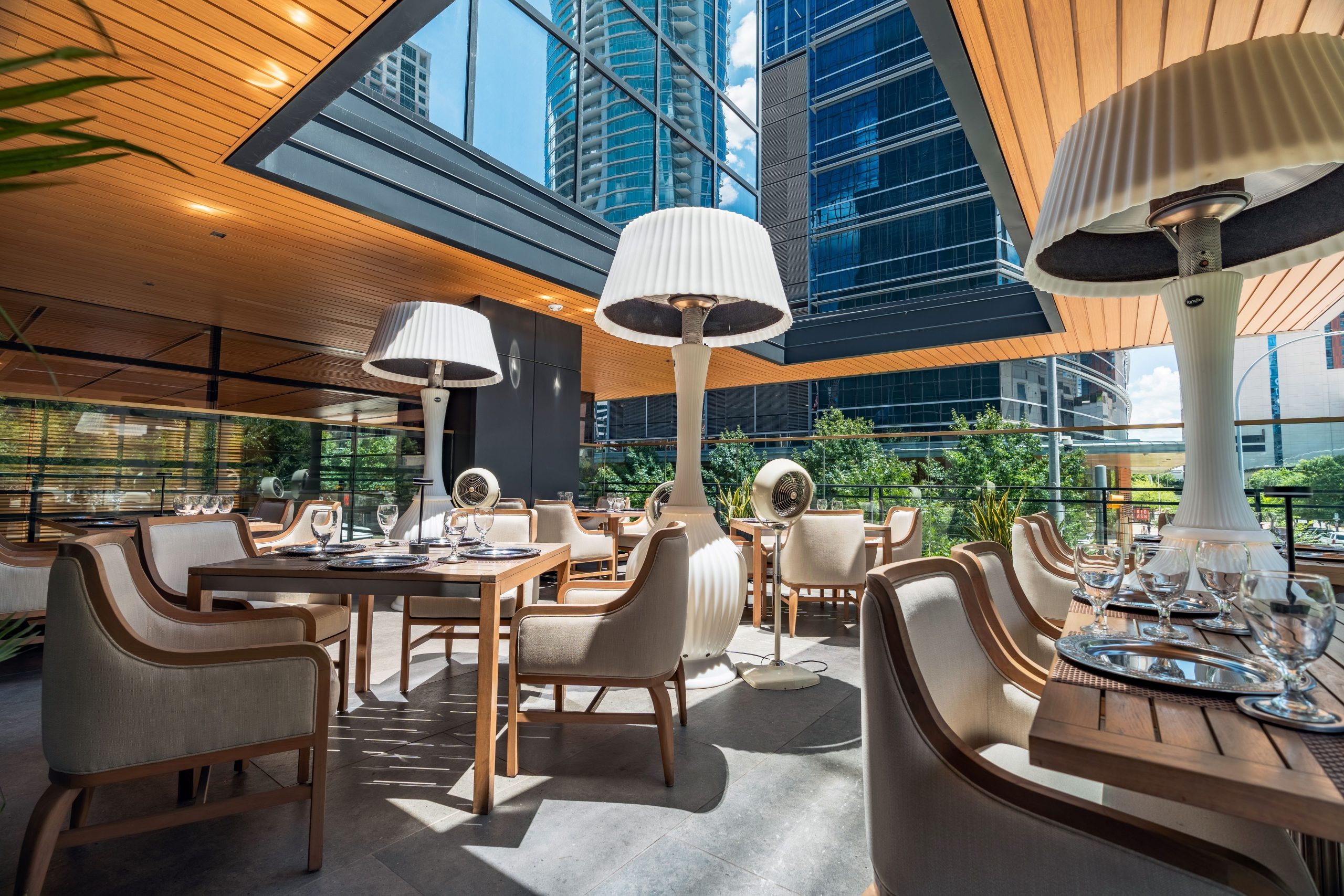 Truluck's Austin downtown outdoor patio during the daytime set with teakwood tables and cushioned wooden resort style chairs.