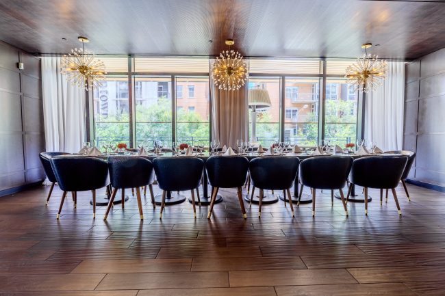 Truluck's Austin downtown upstairs mezzanine with a long boardroom table set up with navy leather chairs and sputnik style chandeliers in front of a large glass window.