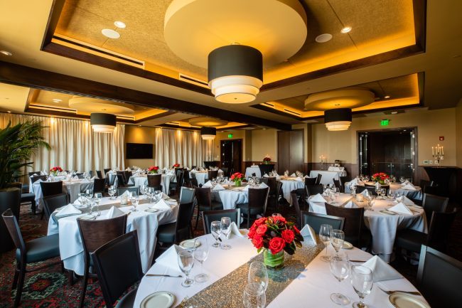 Truluck's Rosemont Stone Crab Room view from the main entry side across the the far rear corner of the room. The tables are dressed in silver runners, candles and flowers.