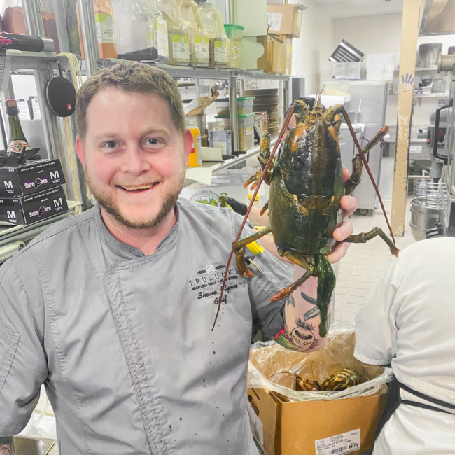 Chef Shane of Trulucks Woodlands holding up a large live lobster in the kitchen