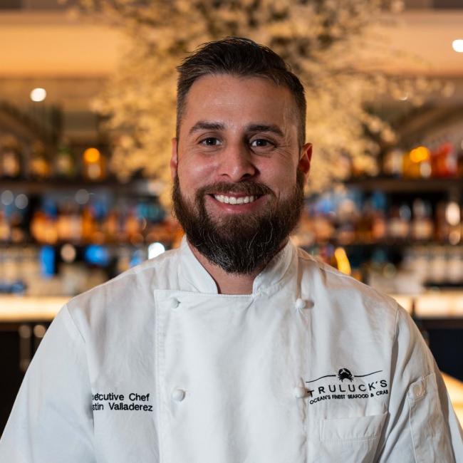 Headshot of Chef Justin of Plano in his chef coat in front of the lit up bar