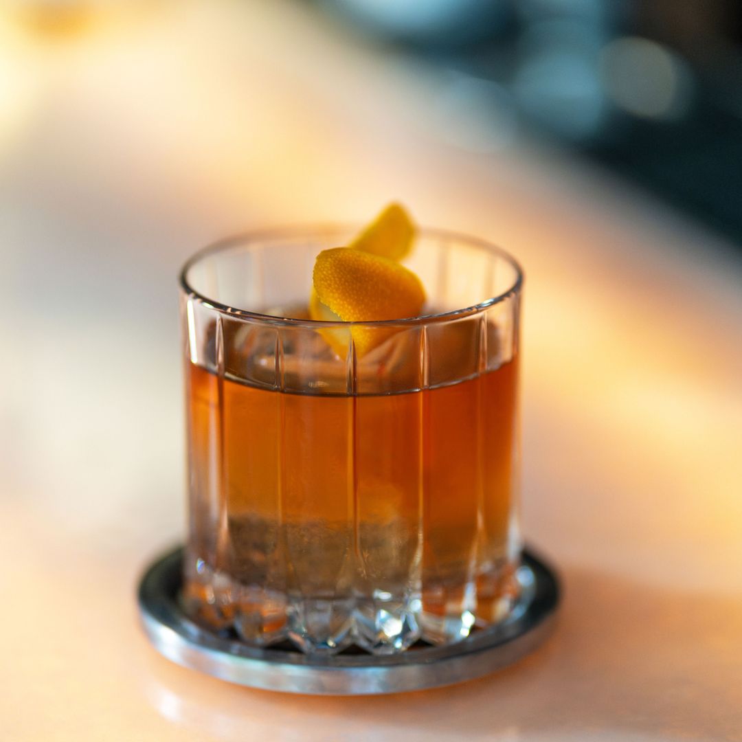 Truluck's reserve old fashioned cocktail in a ridged glass rocks glass sitting on a silver coaster with an orange twist garnish