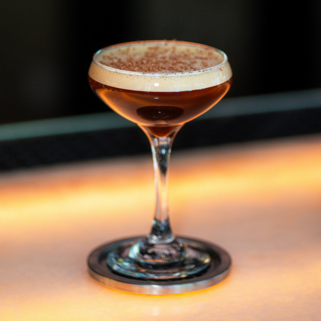 A straight on shot of the espresso martini sitting on a silver coaster on the bartop