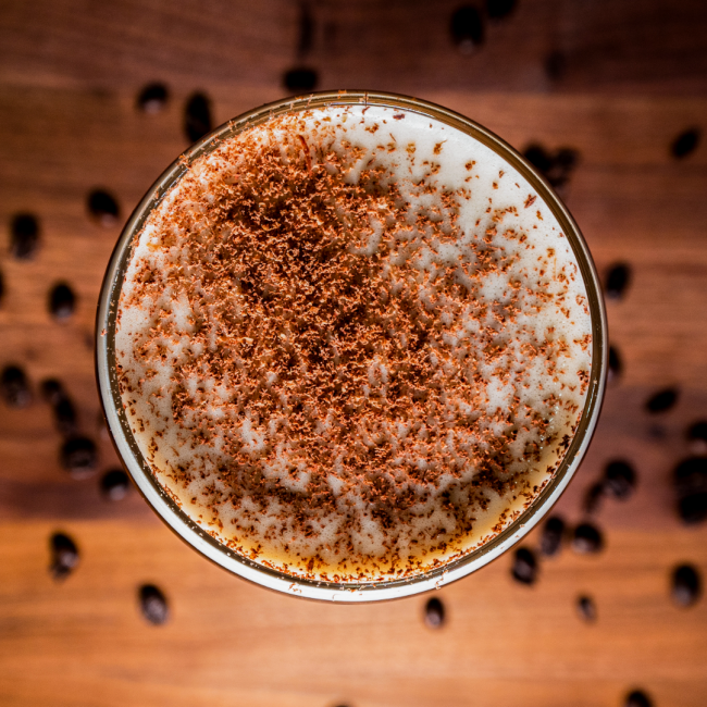 An overhead shot of the espresso martini topped with chocolate shavings. There are fresh beans on the table in the background of the wooden table.