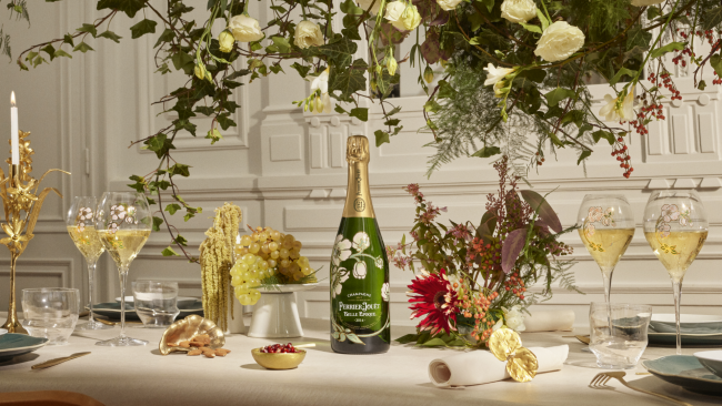 An elegant table setting featuring a bottle of Perrier Jouet Belle Epoque champagne with 4 handpainted glasses filled with champagne, fresh flowers, grapes and a gold candelabra on the table.