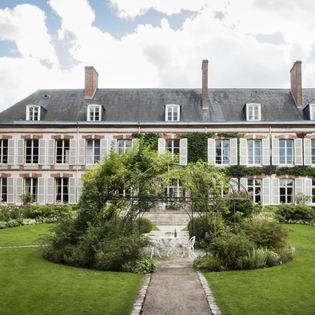 The exterior garden area of House Perrier Jouet in France featuring a table set amongst greenery and set with a bottle of champagne.