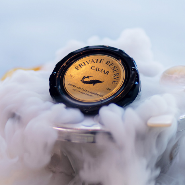 Private reserve caviar in a black and gold tin with dry ice smoke coming out of the container