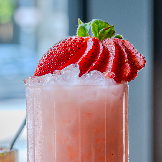 The berry patch zero proof cocktail in a collins glass filled to the top with crushed ice and topped with a whole strawberry sliced into sections and fanned over top.