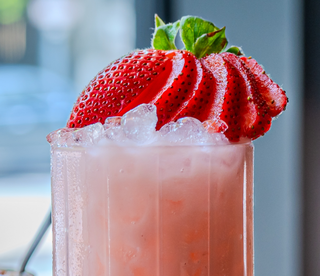 The berry patch zero proof cocktail in a collins glass filled to the top with crushed ice and topped with a whole strawberry sliced into sections and fanned over top.